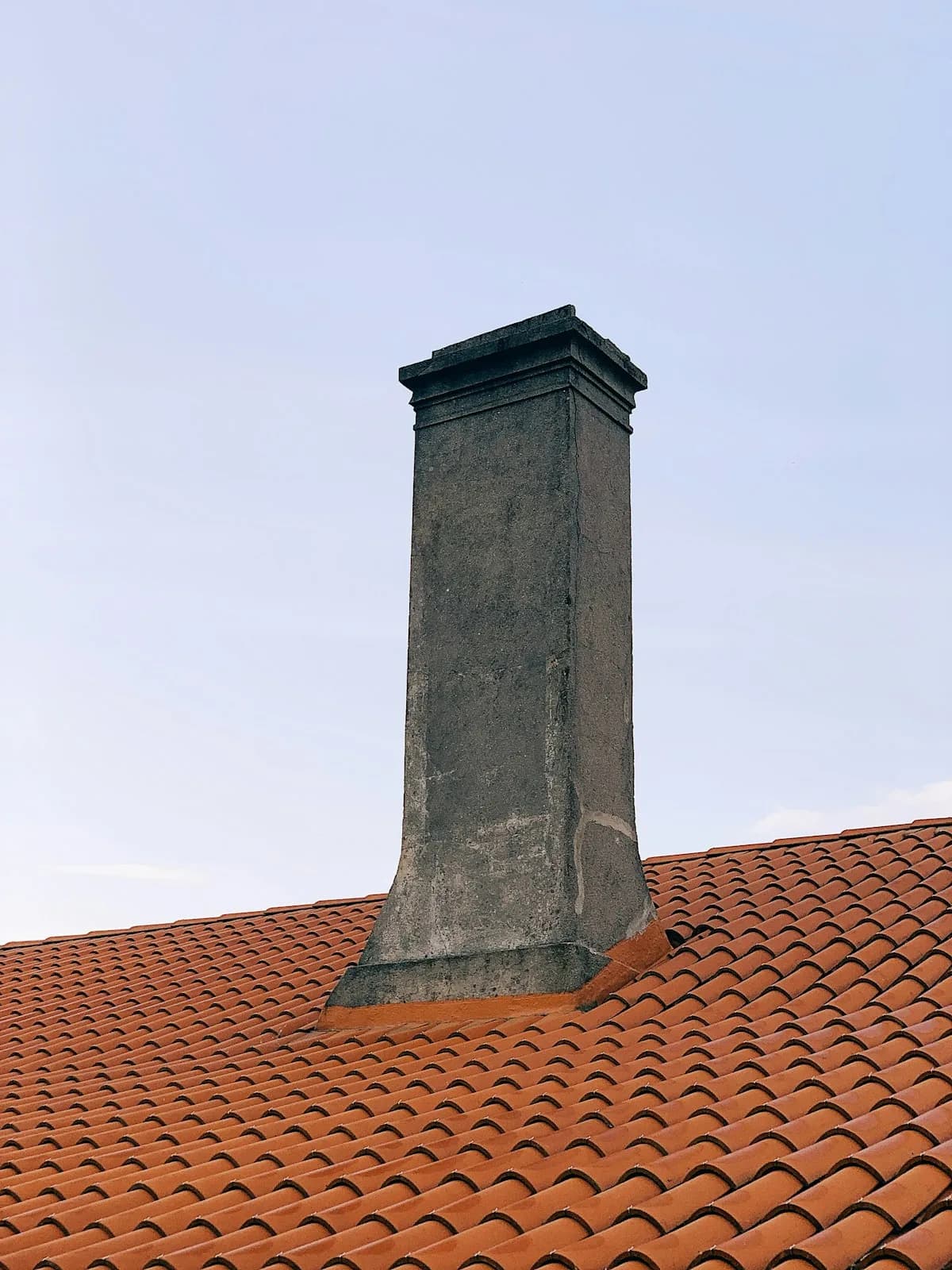 A stuccoed chimney stack with a molded crown on a terracotta tile roof
